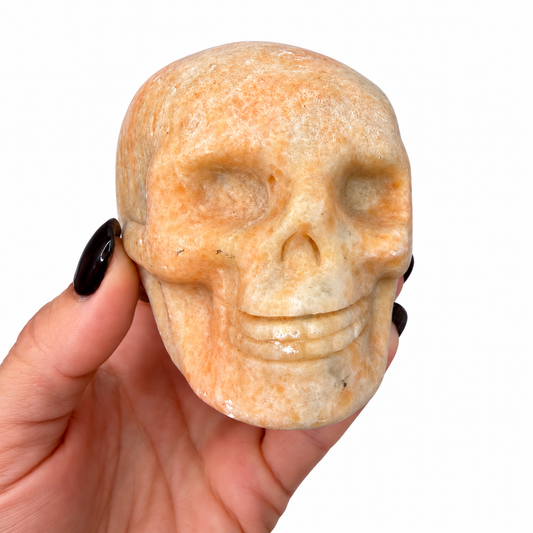 Peach calcite crystal skull, hand carved stone skull next to a quarter for scale - Magick Souls