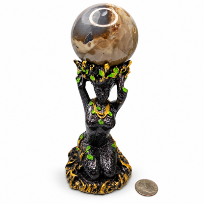 Volcano agate sphere held overhead by black Goddess figure stand with green leaf accents