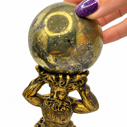 Close-up of polished pyrite sphere with metallic gold shine on God figure stand