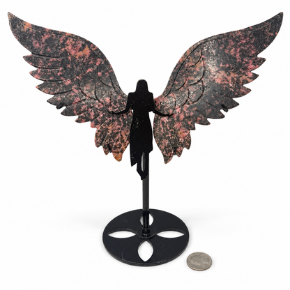 Rhodonite winged goddess, carved pink and black crystal angel wings on black metal goddess stand, next to a quarter for scale - Magick Souls